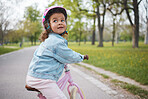 Kids, bike and learning to ride with a girl in the park on her bicycle while wearing a helmet for safety outdoor. Summer, cycling and children with a happy female child training to cycle in a garden