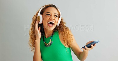 Happy woman, phone and listening with headphones to music and dancing on a gray studio background. Excited female person or model enjoying audio podcast or sound on mobile smartphone or mockup space