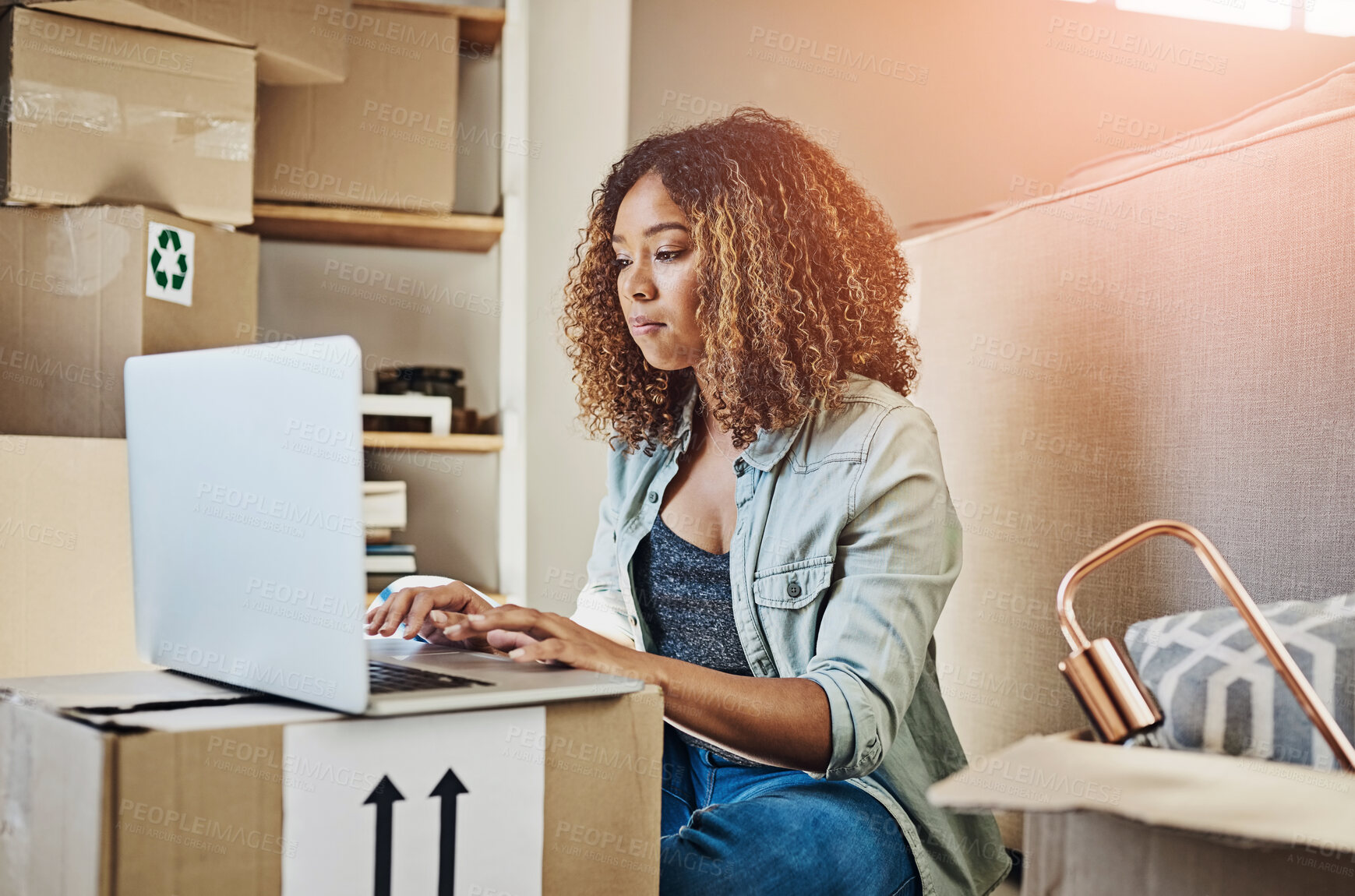Buy stock photo Shot of a focused young woman working on a laptop while seated on the floor and with boxes all around her at home