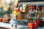 Christmas, trolley and miniature gifts on laptop for celebration, festive season or religious holiday. Closeup, presents and shopping cart on computer for xmas, surprise and wrapping paper with bokeh