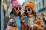 Women, friends and smartphone in city for online shopping in winter, big discount on fashion with app. Female people and walking with mobile in urban for communication, purchase with technology