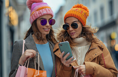 Women, friends and smartphone in city for online shopping in winter, big discount on fashion with app. Female people and walking with mobile in urban for communication, purchase with technology