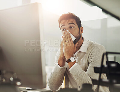 Buy stock photo Shot of a handsome young businessman blowing his nose while working late in an office