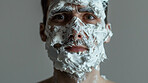 Man, portrait and studio with shaving cream to cover face for grooming, hiding and fear with cleaning by background. Model, person and foam for beard, routine and facial hair removal with anxiety