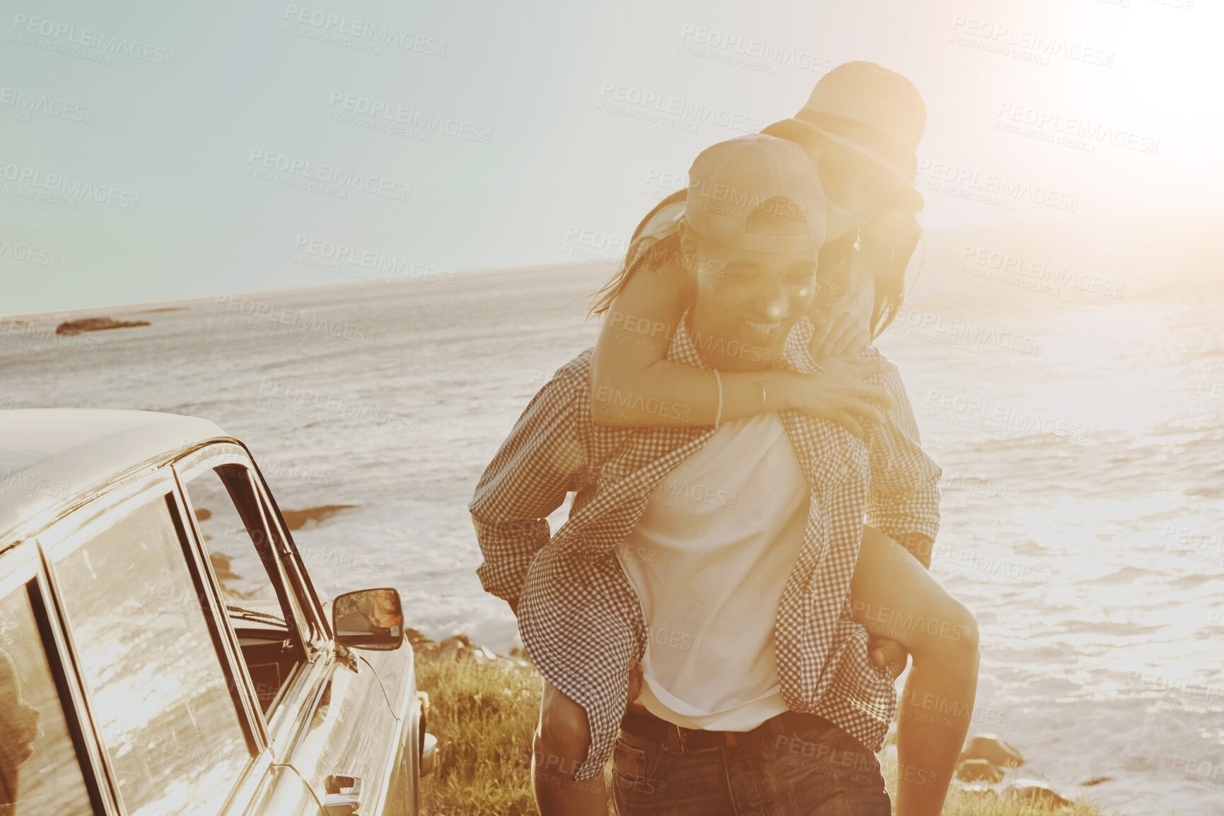 Buy stock photo Happy couple, sunset and piggy back by ocean with car, smile or road trip on holiday adventure in summer. Man, woman and connection for love, playful or memory for bonding in sunshine by sea in Italy