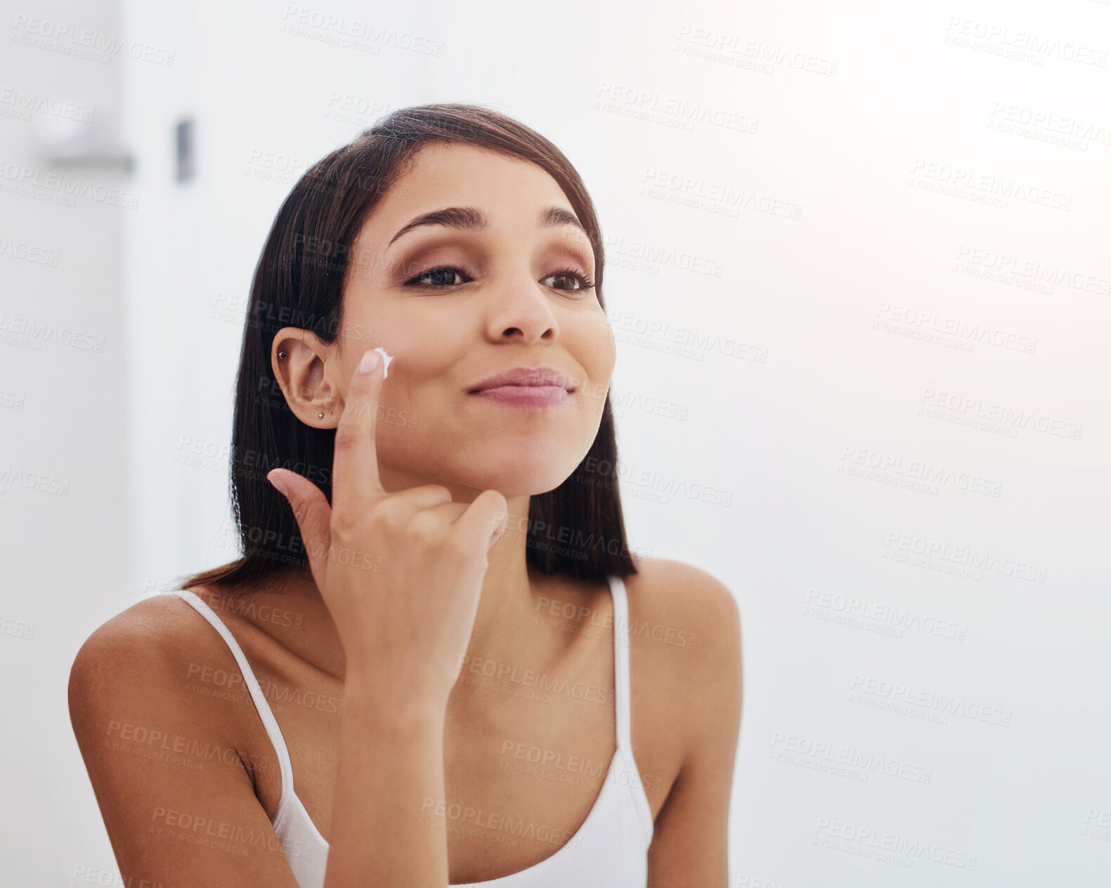 Buy stock photo Shot of an attractive young woman applying moisturizer to her face in the bathroom