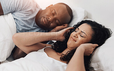 Buy stock photo Shot of an uncomfortable looking young woman holding her ears closed because of her husband's snoring in bed at home