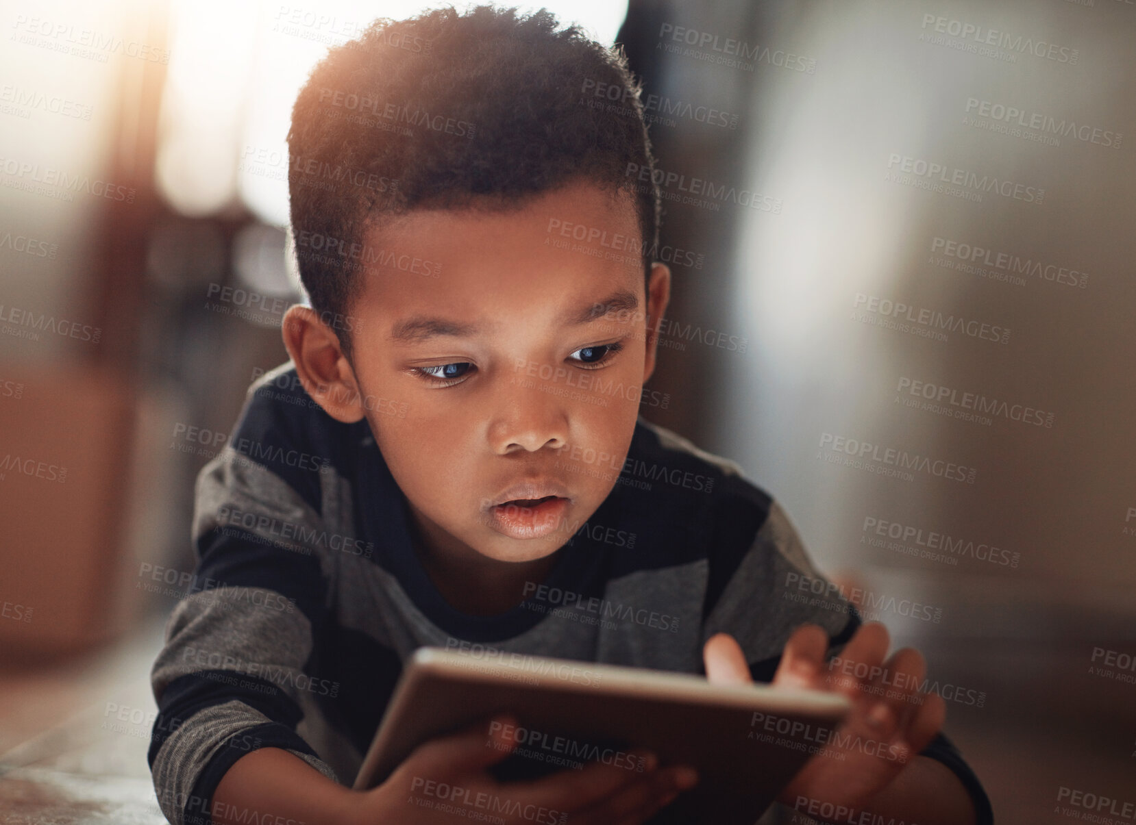 Buy stock photo Shot of a young boy using his digital tablet while lying on the floor at home
