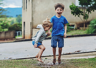 Buy stock photo Portrait of two cheerful young children jumping around in mud outside during a rainy day