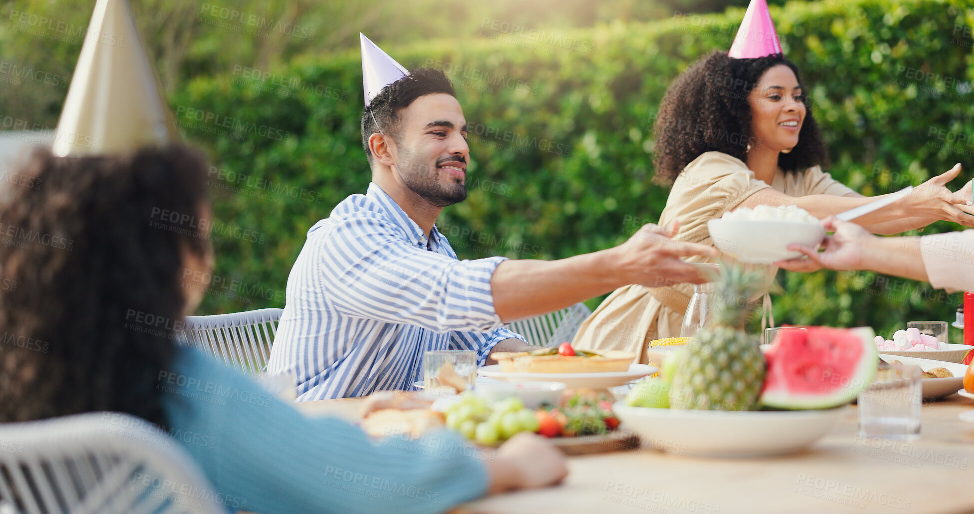 Buy stock photo Family, eating and happy with conversation at birthday party for celebration, surprise or hat in garden of home. Couple, parents and kids with drinks for gathering and event in backyard of house