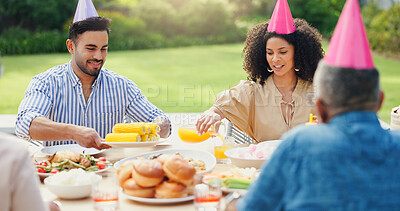 Family, men and women at birthday party in garden with hat, happy and giving food at brunch in summer. People, relax and holiday with celebration, event and together for eating corn in home backyard