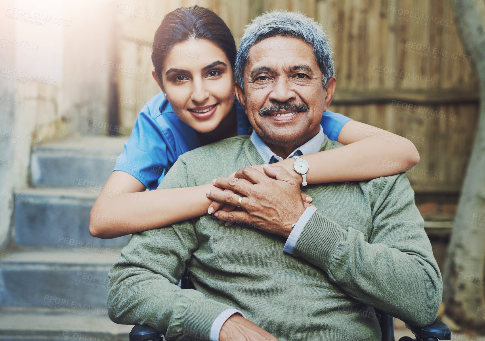 Buy stock photo Portrait of a cheerful young female nurse holding a elderly patient in a wheelchair as support outside during the day