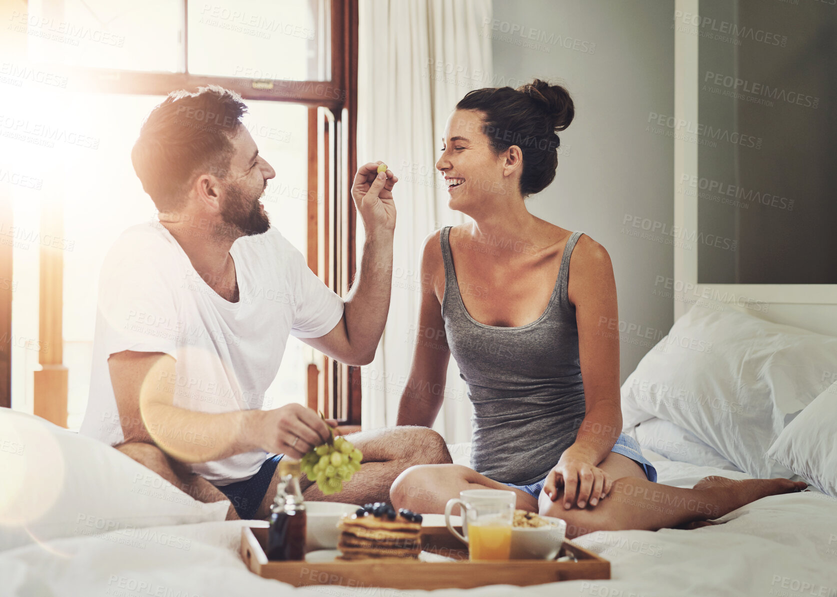 Buy stock photo Feeding, morning or couple with breakfast in bed for wellness, brunch or food together to relax in home. Romantic, wake up or people eating for healthy diet, love or drinking coffee on valentines day