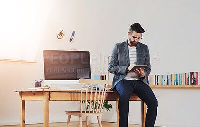 Buy stock photo Cropped shot of a handsome young businessman working on a tablet while sitting in his home office