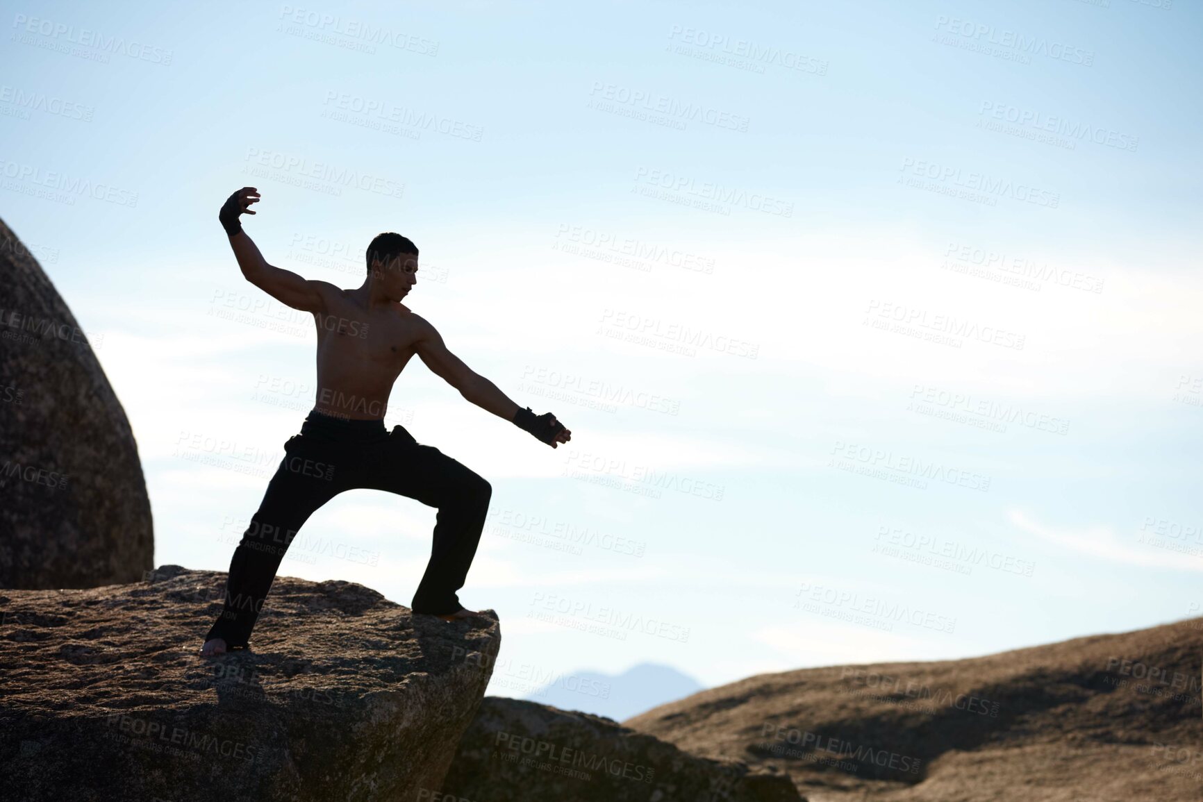 Buy stock photo A male athlete kickboxing on the edge of a cliff on a mountain