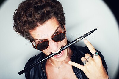 Buy stock photo Rock man, horns and studio portrait with drumstick, sunglasses or biting in spotlight by white background. Punk musician, drummer or artist with emoji, icon and hand sign for performance at concert