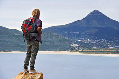 Buy stock photo Man, backpack and hiking on mountain by ocean for travel, sightseeing or outdoor journey in nature. Rear view of male person, hiker or tourist with bag on rock for trekking, fitness or adventure