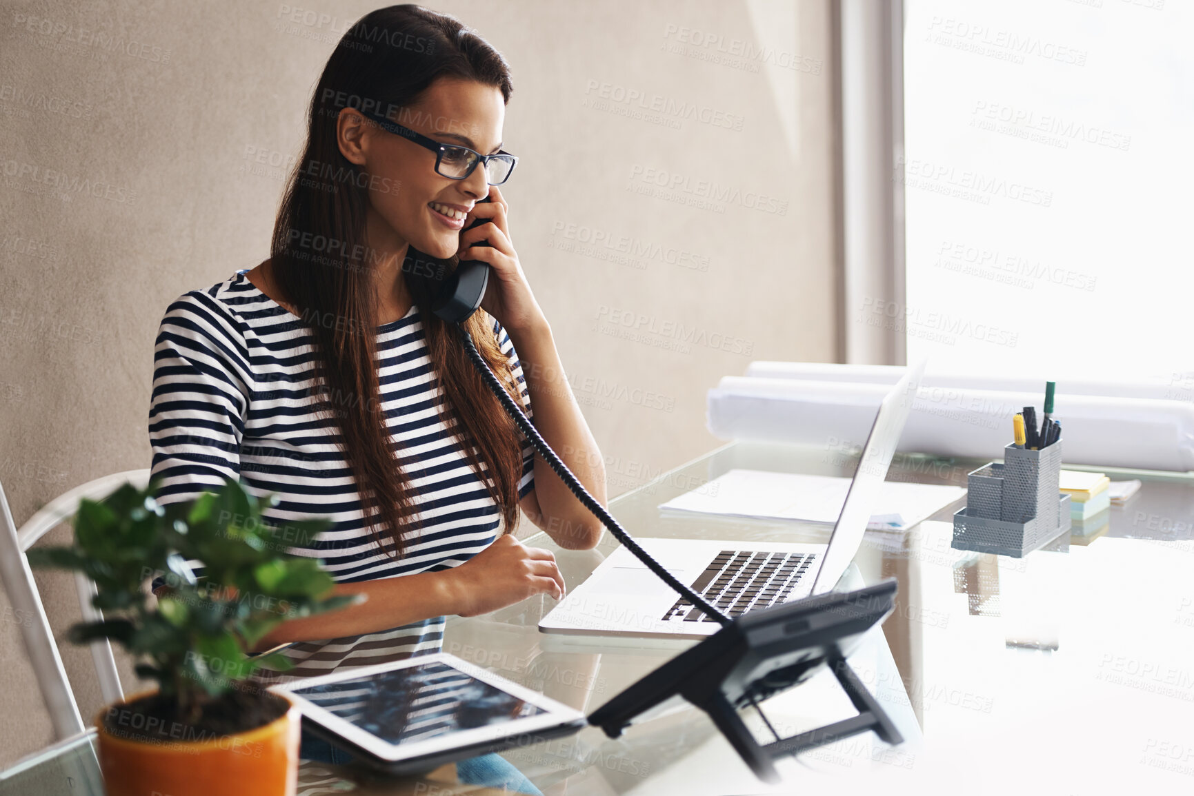 Buy stock photo Shot of a young businesswoman talking on the phone while working on her laptop