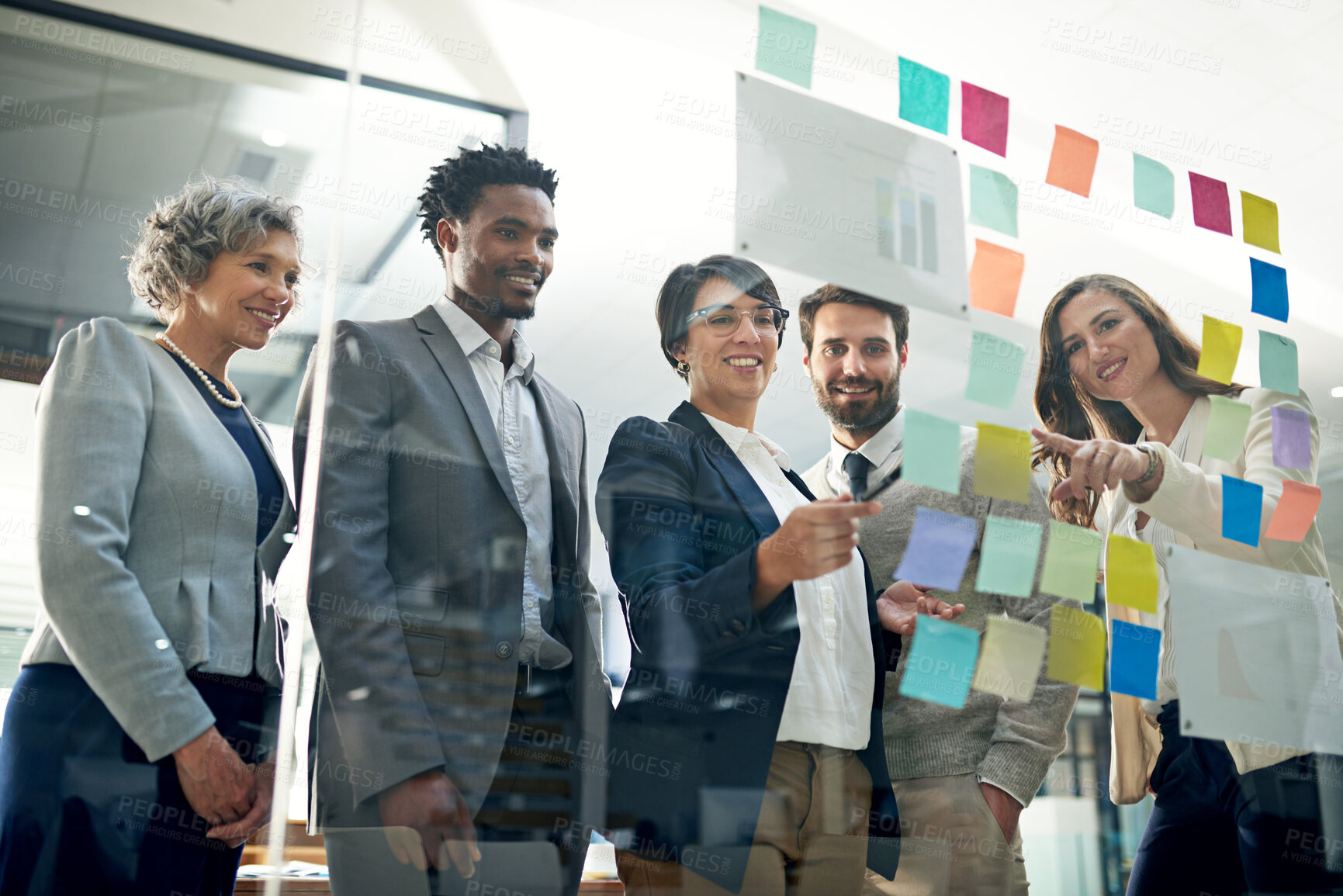 Buy stock photo Shot of a group of businesspeople brainstorming on a glass wall in an office