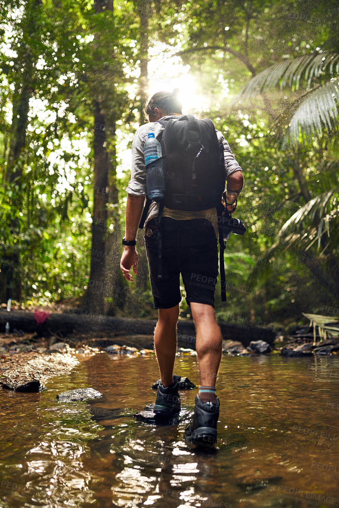 Buy stock photo Rearview shot of an unidentifiable hiker crossing a stream while exploring in the woods