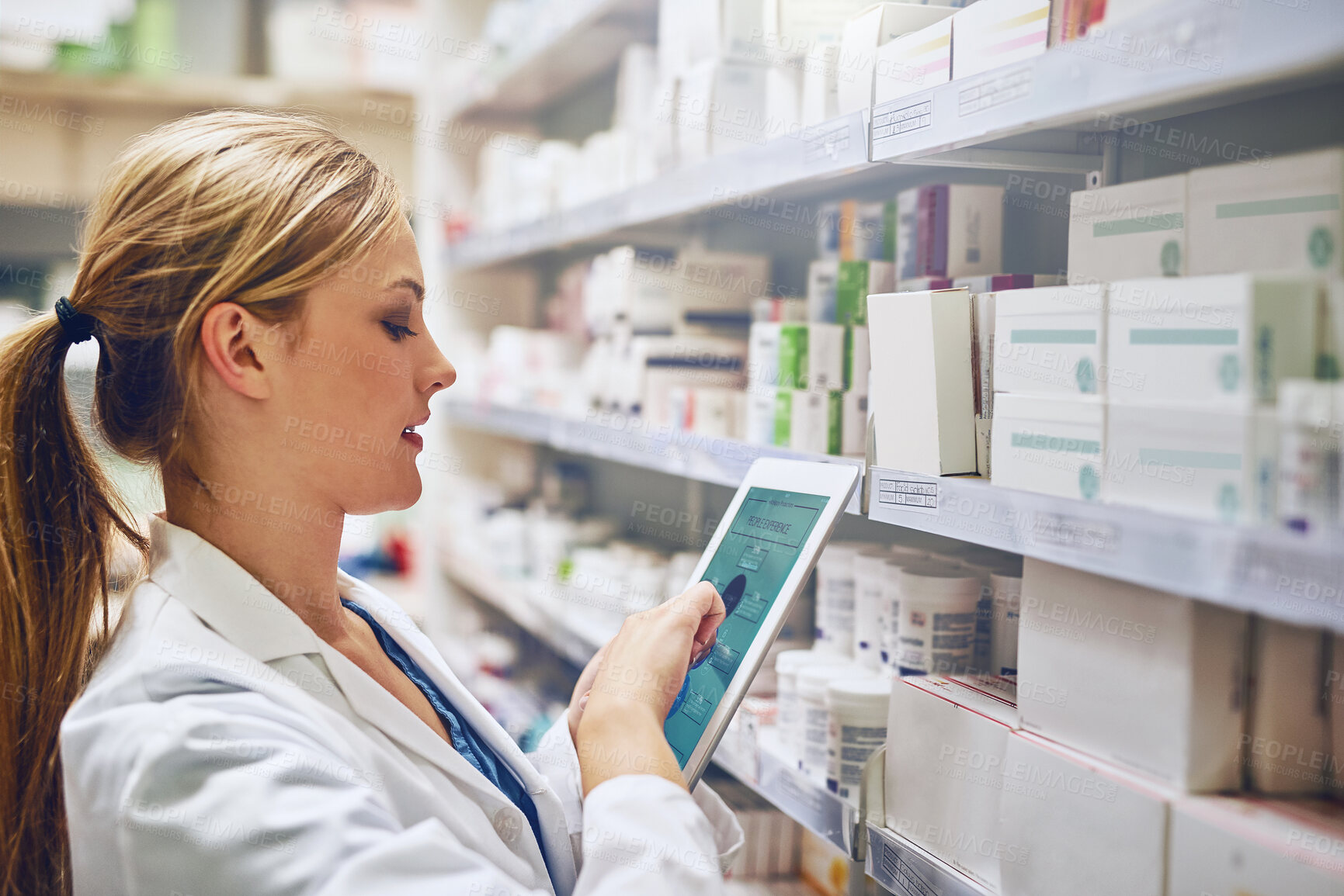 Buy stock photo Shot of a pharmacist using her digital tablet while working in a isle