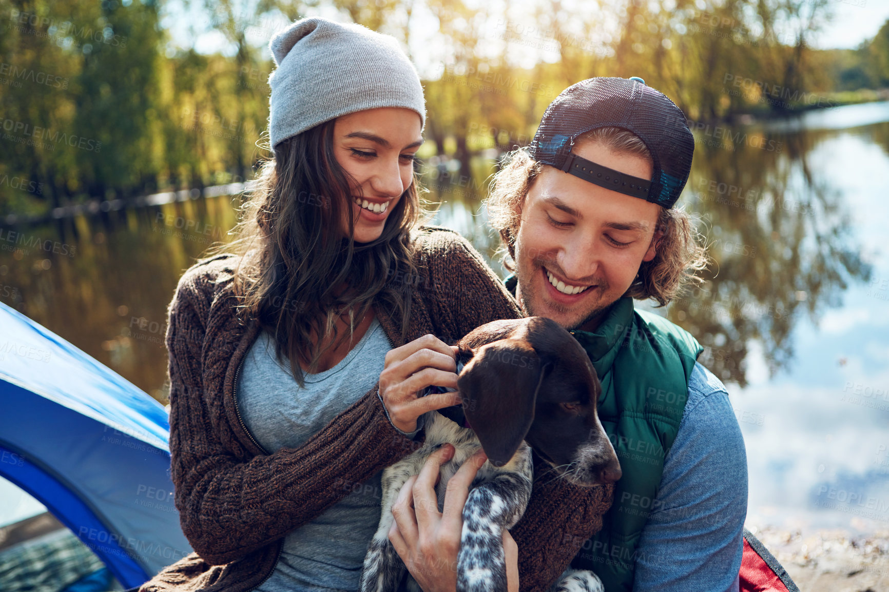 Buy stock photo Dog, camping or couple on adventure with love of animal for freedom in nature, sunshine or smile at lake, travel or holiday. Happy, woman or man with puppy pet to care, hug or relax on summer journey