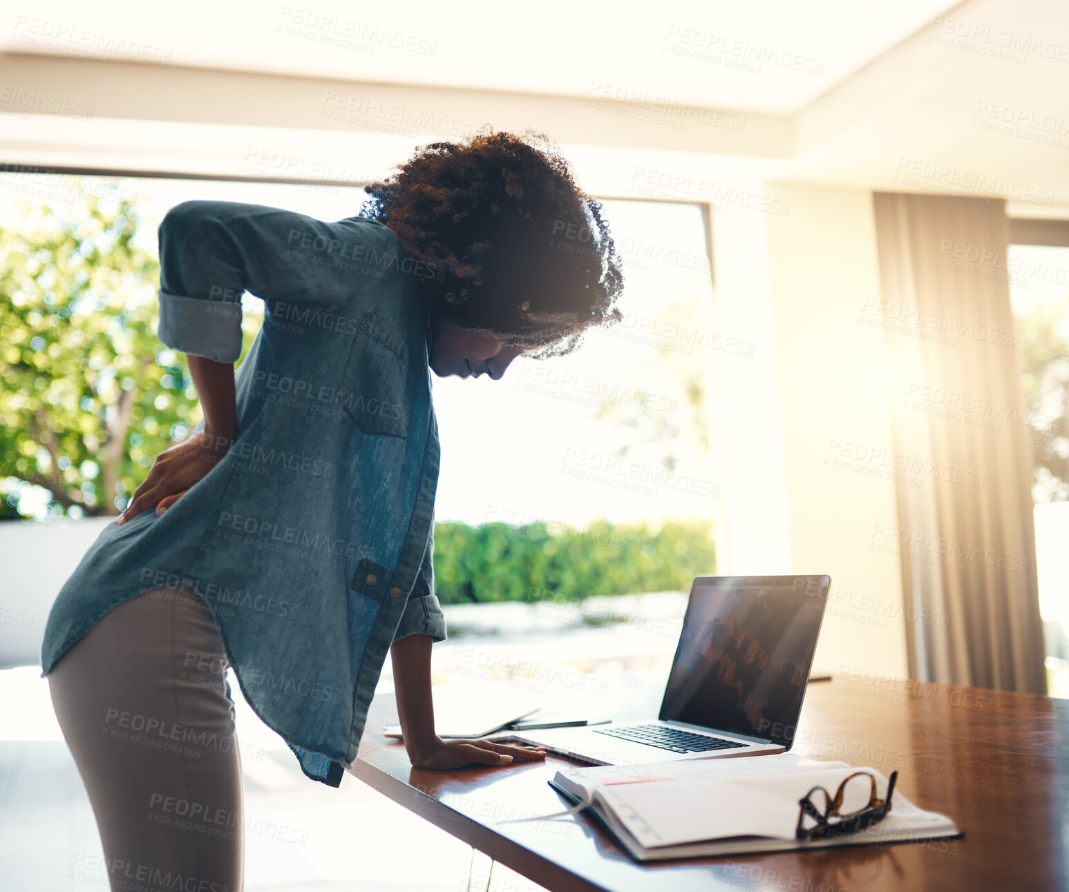 Buy stock photo Shot of a young woman holding her back in pain while getting up from her desk at home