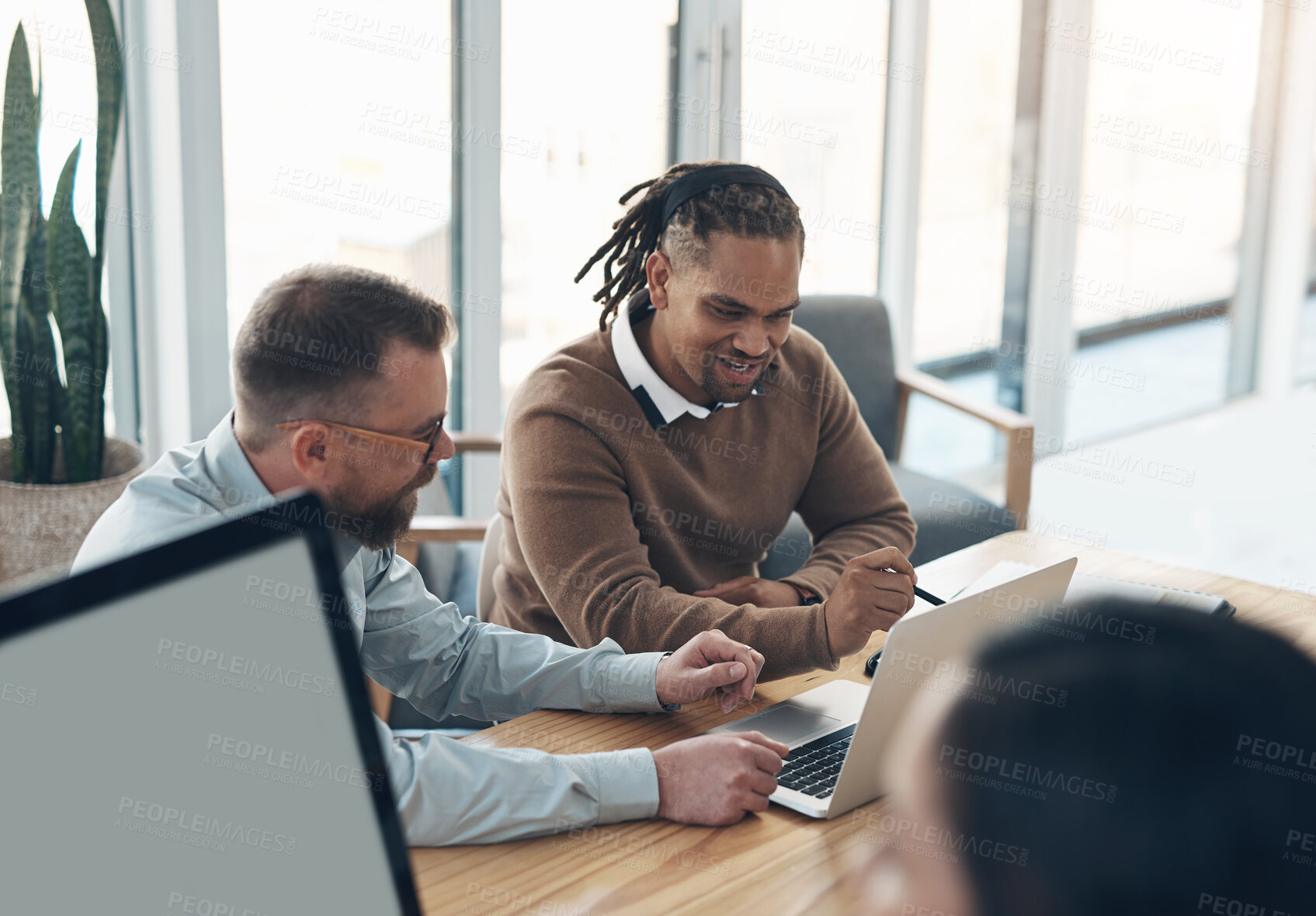 Buy stock photo Cropped shot of two handsome businessmen sitting and using a laptop in the office while their colleagues work around them