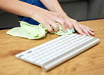 Hands, keyboard and cloth with a person cleaning a keyboard on a wooden desk for hygiene. Technology, health and sanitize with an adult wiping a wireless device on a table for safety