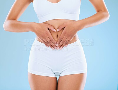 Buy stock photo Woman, heart and hands on stomach in studio for gut health, digestive wellness and nutritional balance for digestion. Girl, love gesture and isolated on blue background for body care and weightloss.