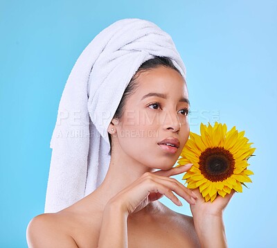 Buy stock photo Woman, sunflower and beauty with skincare in studio for organic wellness, glow or health by blue background. Girl, model and thinking for dermatology with natural makeup, plant or cosmetic with towel