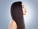 Profile view of a beautiful brown-haired girl with smooth and shiny hair posing against a grey background. Young brunette woman with beautiful long straight hair