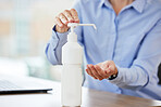 Closeup of female hands using sanitiser at workplace. Bottle of alcohol gel placed on desk in office to clean hands and kill or prevent spread of germs during coronavirus outbreak