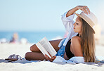 One beautiful young caucasian woman relaxing on the beach. Enjoying a summer vacation or holiday outdoors during summer. Taking time off and getting away from it all. Reading alone on the sand outside