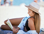 One beautiful young caucasian woman relaxing on the beach. Enjoying a summer vacation or holiday outdoors during summer. Taking time off and getting away from it all. Reading alone on the sand outside