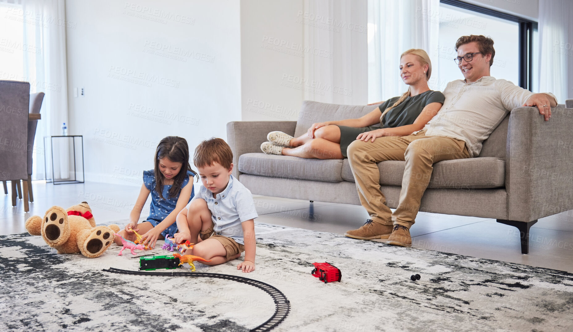 Buy stock photo Parents on sofa, happy and watch children with toys on the living room floor and home. Mom relax with dad on couch in lounge, as boy and girl kids have fun together on carpet in family house