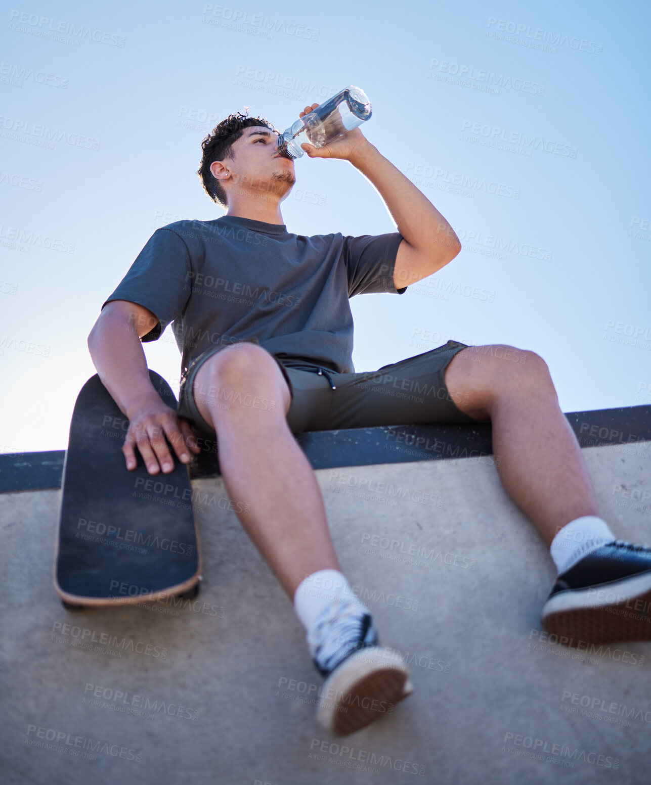 Buy stock photo Skateboard, young man and drinking water bottle, relax and on break on sunny day outdoor. Male, skater and athlete hydrate, thirsty and sports for wellness, health and have fun in summer.