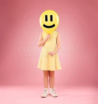 Buy stock photo Emoji face, balloon and child in studio, covering and hiding against a pink background space. Happy, smile and girl holding toy, game and playing while posing behind inflatable, fun and innocent