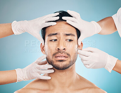 Buy stock photo Face, hands and plastic surgery with a worried man in studio on a blue background for beauty enhancement. Aesthetic or change with a young male patient looking nervous in a clinic for skincare