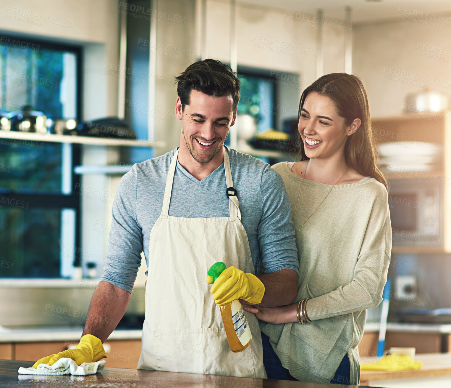 Buy stock photo Happy, couple and cleaning with bottle in kitchen for hygiene, teamwork and support in maintenance. Man, woman and smile with detergent at home for bacteria removal, housekeeping and help in marriage