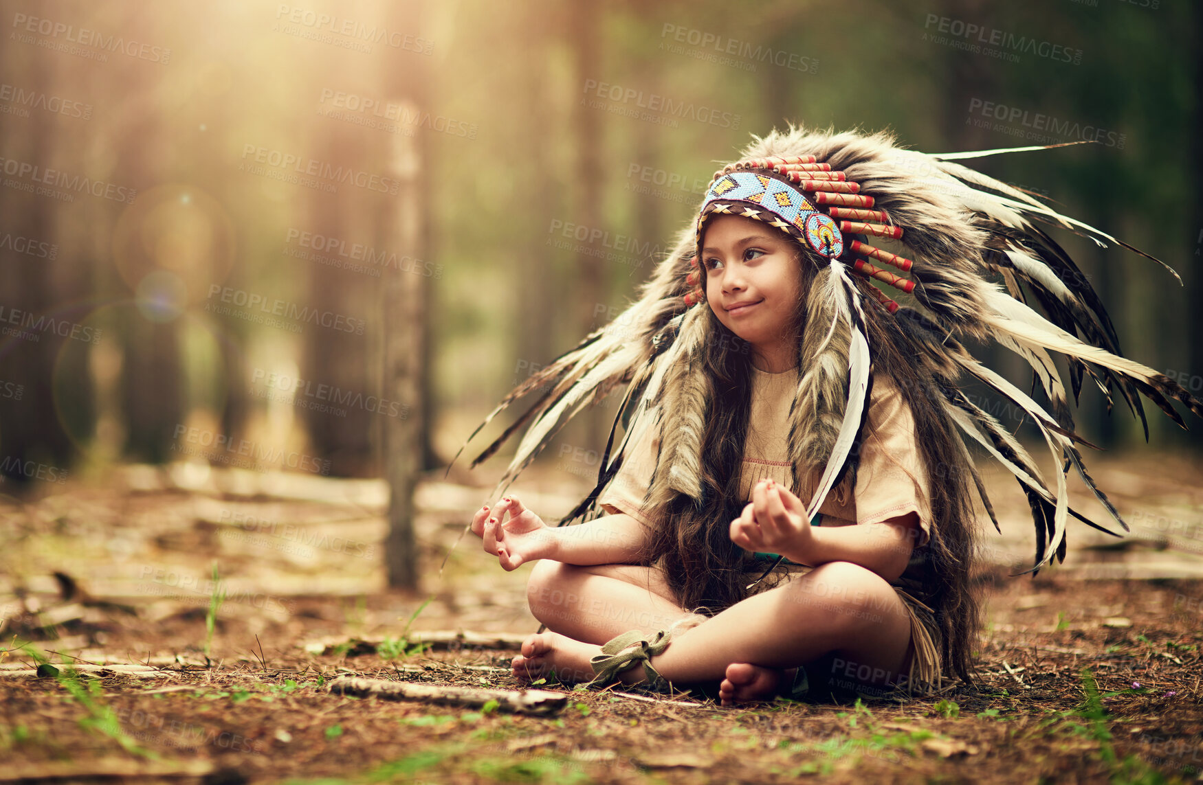 Buy stock photo Nature, forest and child in Native American costume for meditation, tradition and culture. Trees, relax and kid on floor in woods with feather head gear, indigenous cosplay and outdoor childhood fun.