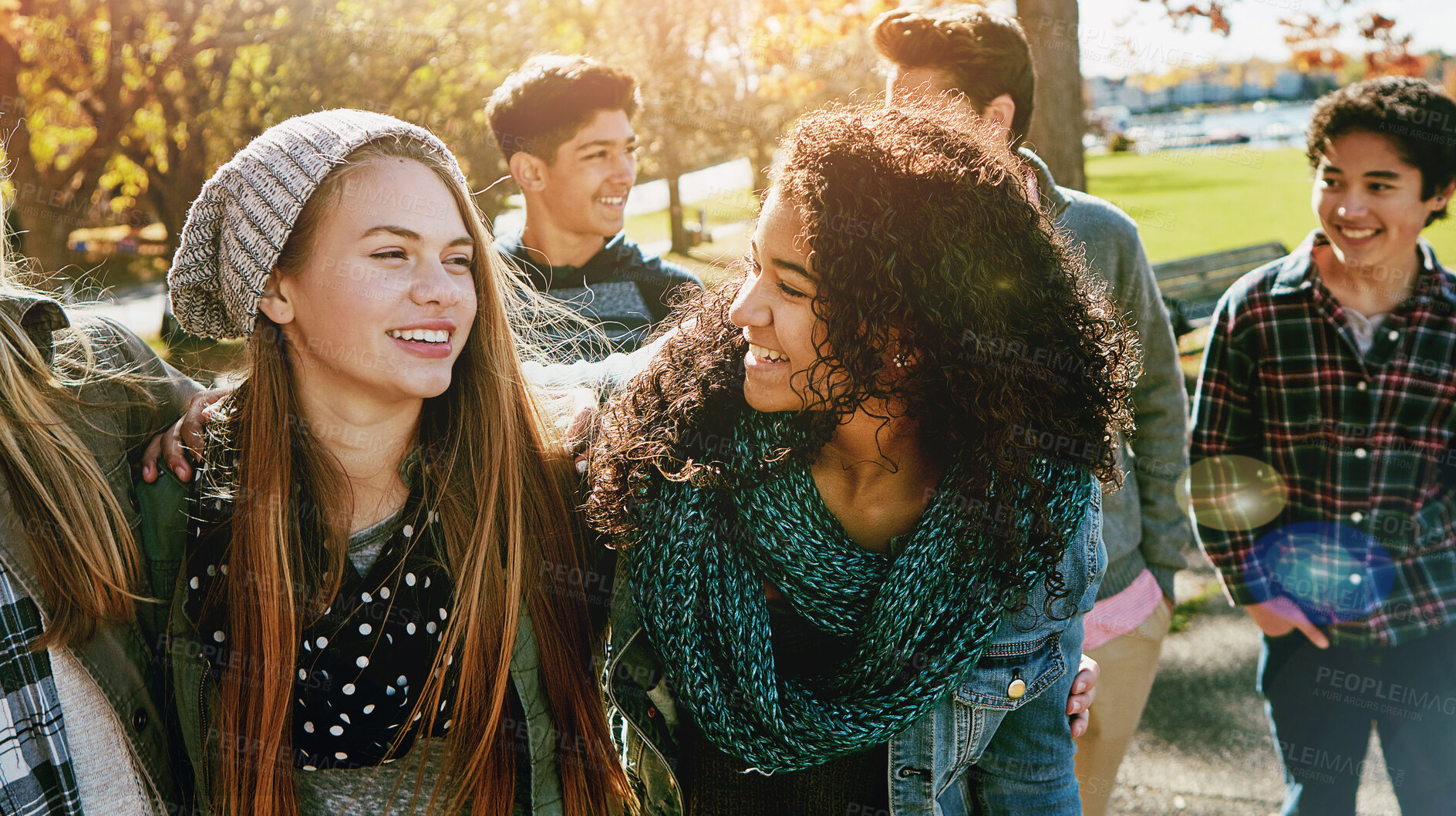 Buy stock photo Teenage girls, laughing and walking in nature for fall break, hangout together and sunshine. Boy group, happy friends and hug at park for bonding, weekend stroll and funny conversation with support