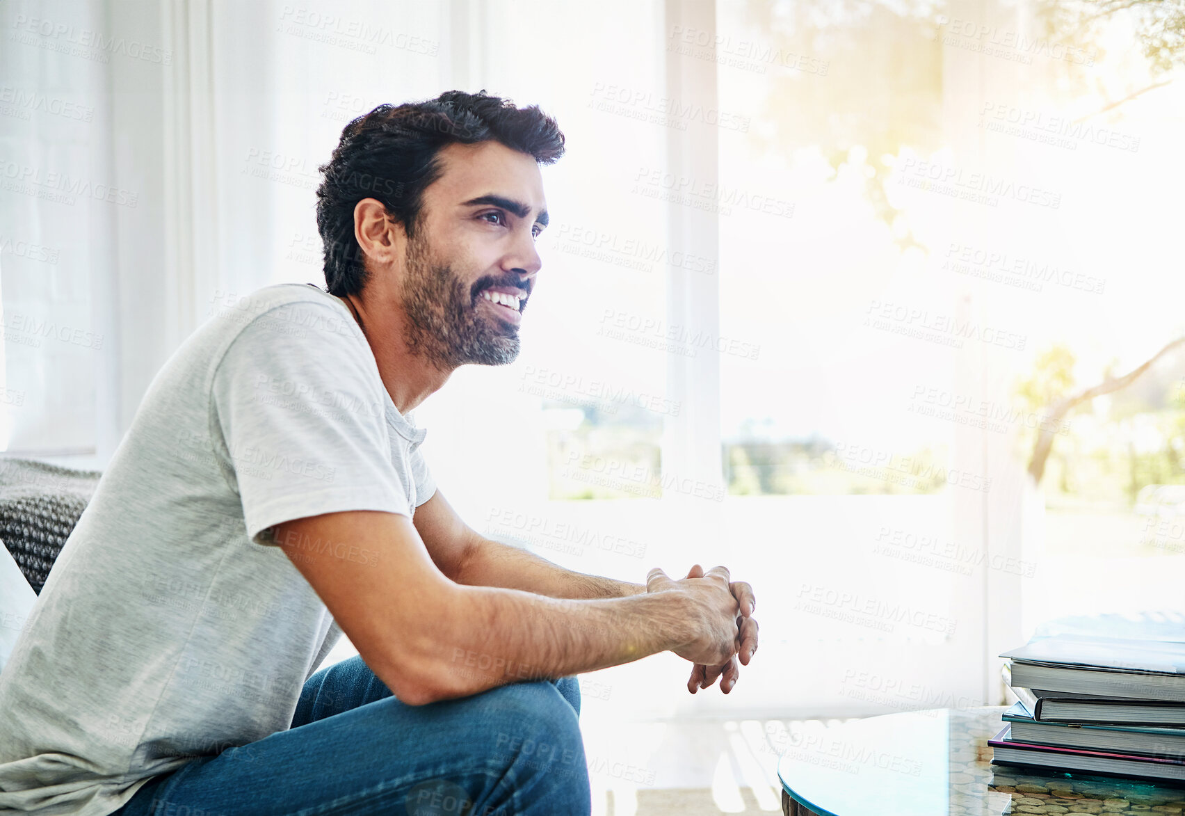 Buy stock photo Relax, home and thinking with man, smile and ideas with sunshine, weekend break and wonder. Happy person, apartment and guy in living room, thoughts and chilling with lens flare, peaceful and calm