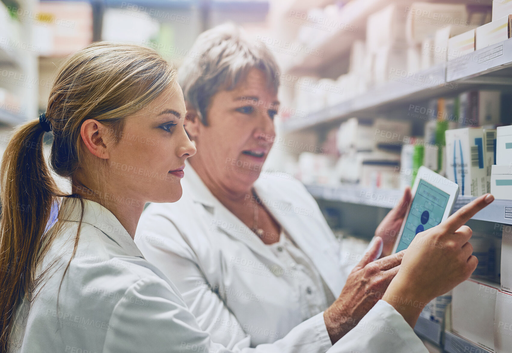 Buy stock photo Pharmacist, women and together with tablet by shelf for stock, check and inventory with pointing in shop. People, mentor and intern with digital touchscreen, app and inspection for drugs at store