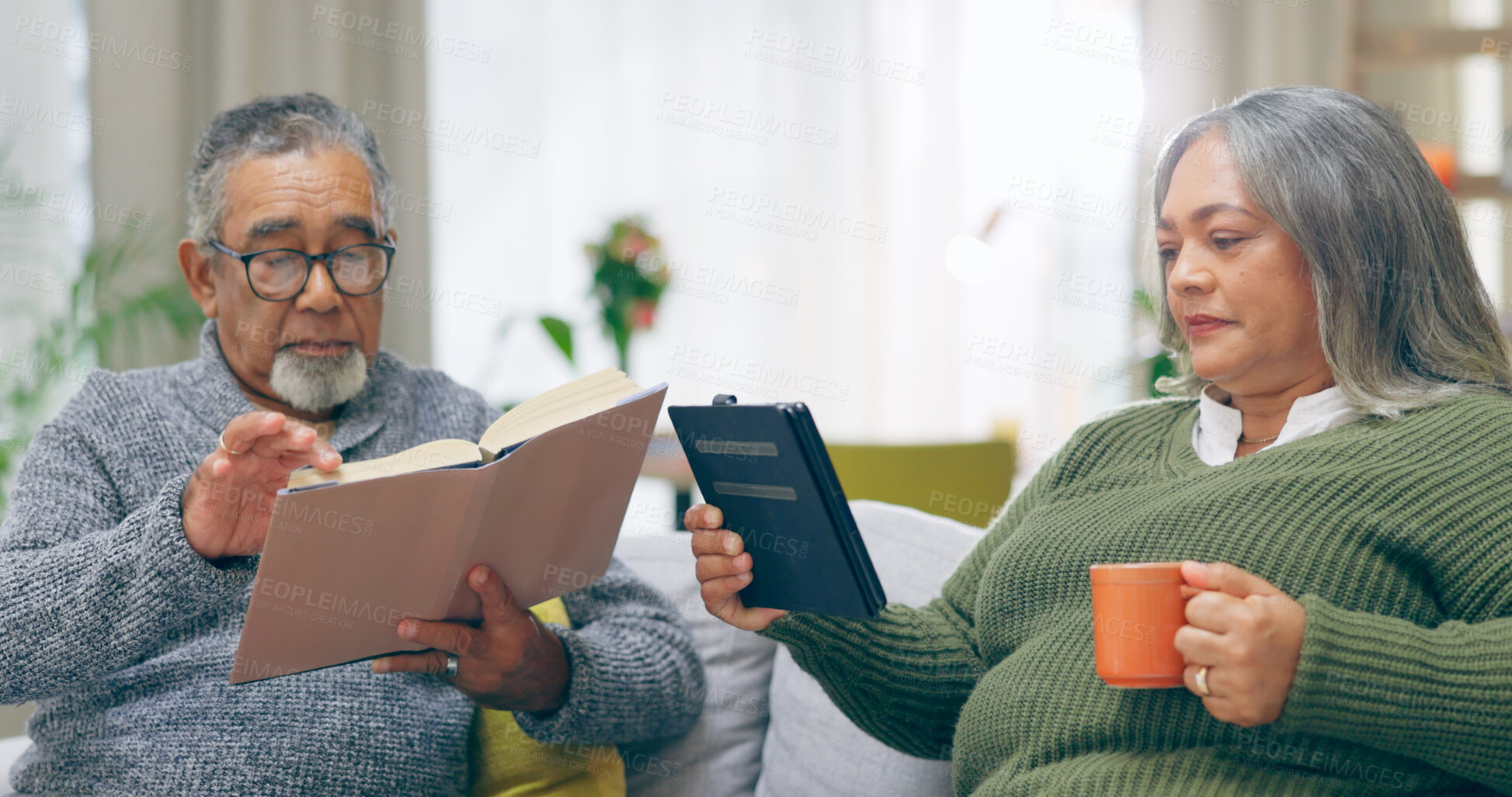 Buy stock photo Reading, relax and senior couple on a sofa with book, tablet and coffee while bonding at home together. Literature, ebook and old people chilling with tea in a living room calm and enjoy retirement