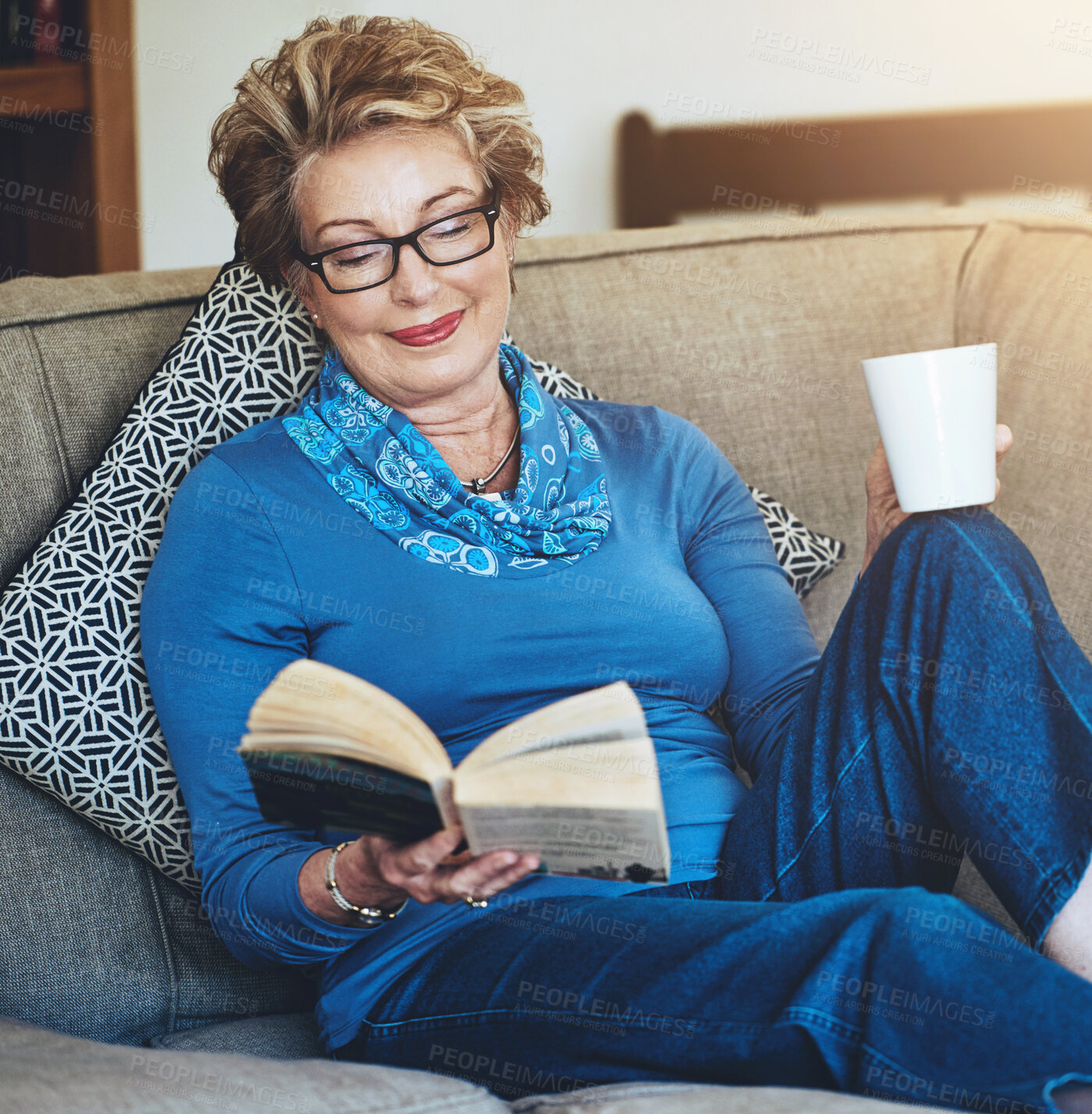 Buy stock photo Senior woman, glasses and reading book or story on sofa with coffee for funny literature in retirement. Grandma, novel and drink on couch for rest, relax and comfort with hobby for entertainment