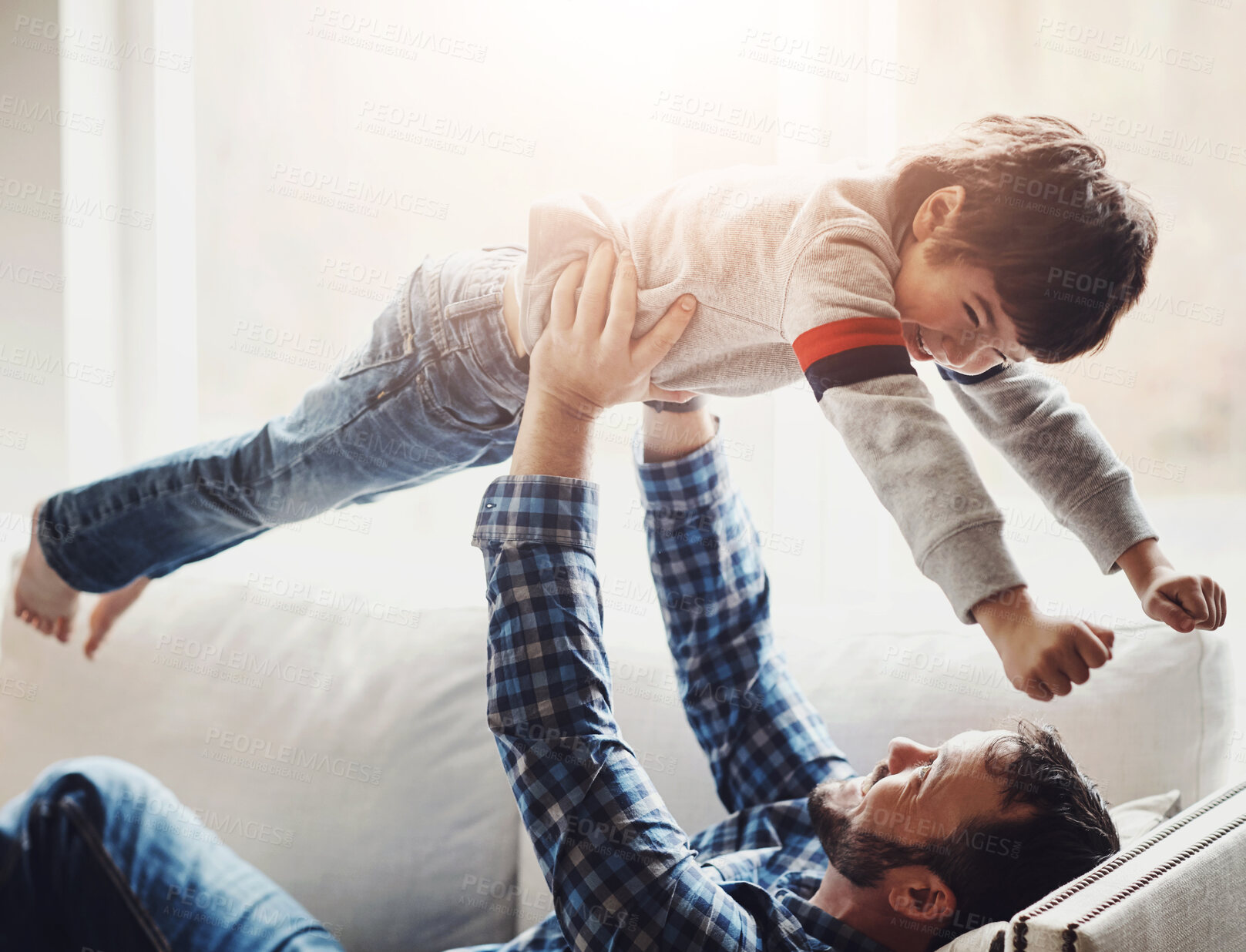 Buy stock photo Father, boy and lifting child on sofa  with fun for bonding, airplane and playing together in living room. Strong man, lens flare and young kid flying in air for support, game and happiness in home
