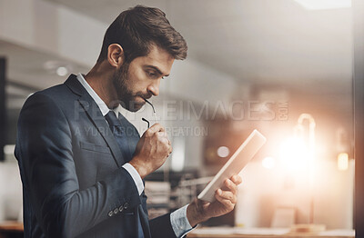 Buy stock photo Shot of a young businessman using a digital tablet while working late in an office
