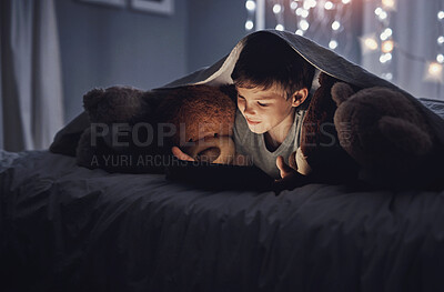 Buy stock photo Shot of an adorable little boy using a digital tablet in bed at night