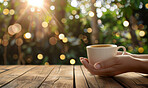 Woman, coffee and closeup with hands and bokeh in garden, trees with wood table and drink. Female person, espresso or milk in restaurant by table for winter, barista with inspiration in Chicago